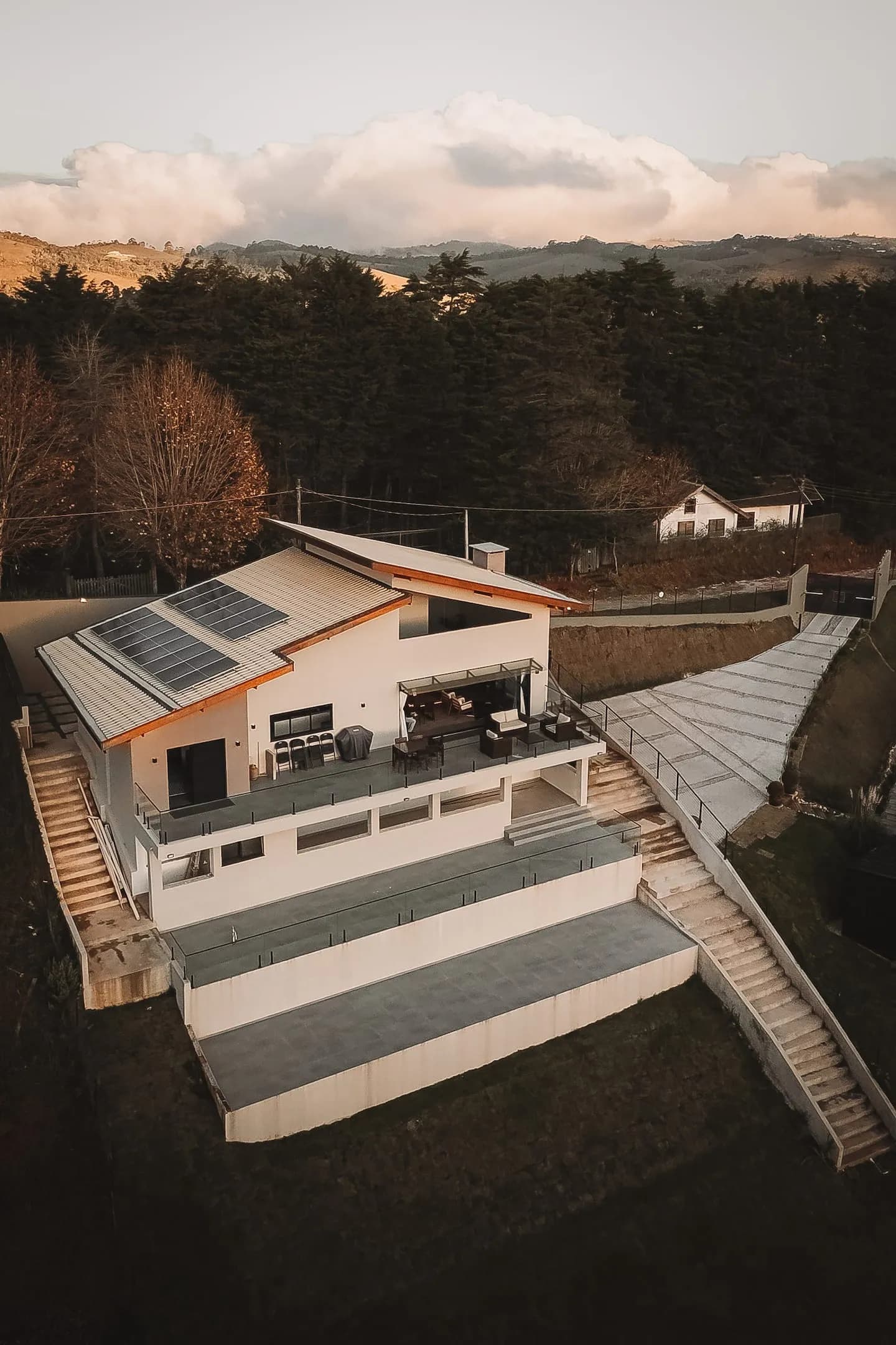 Vista aérea da casa e do terreno com luz de fim de tarde sobre as colinas