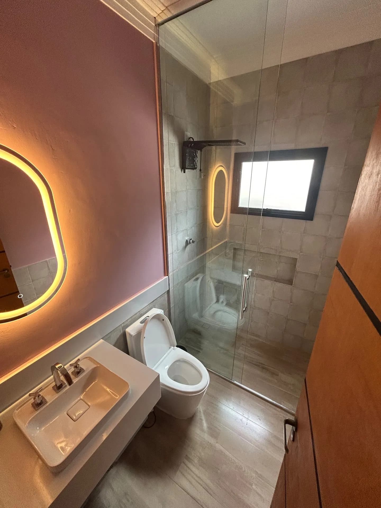 Banheiro de suíte com espelho de contorno luminoso e chuveiro de vidro
