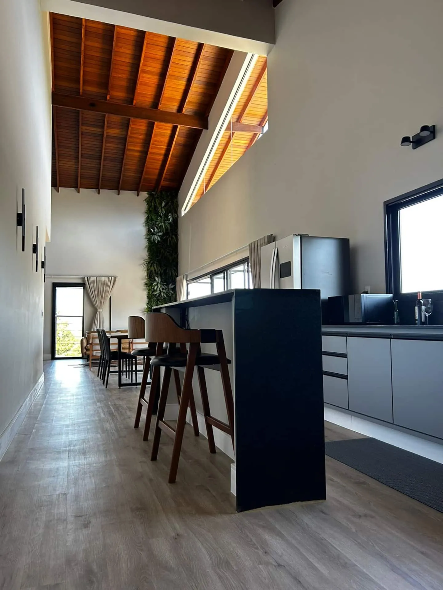 Corredor da casa com cozinha à direita e teto de madeira