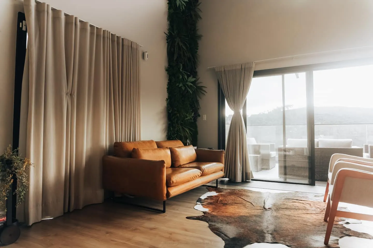 Sofá de couro caramelo ao lado das cortinas e da vista para a serra