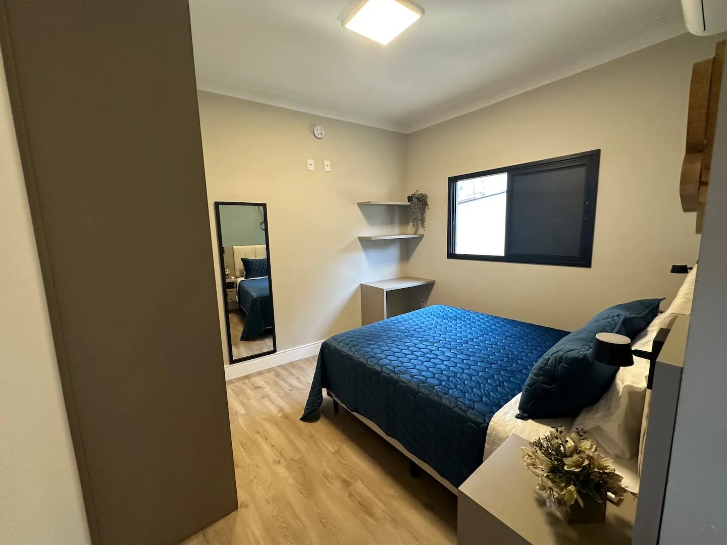 Suíte com cama queen de colcha azul e espelho de corpo inteiro