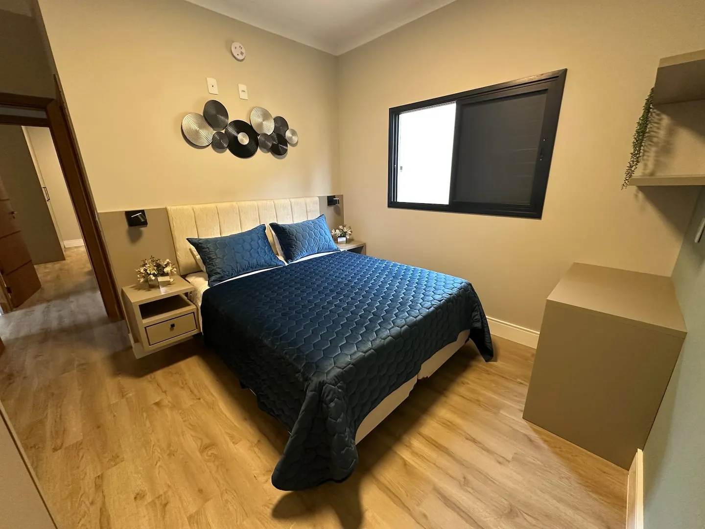 Suíte com piso de madeira, cama queen e painel decorativo na parede