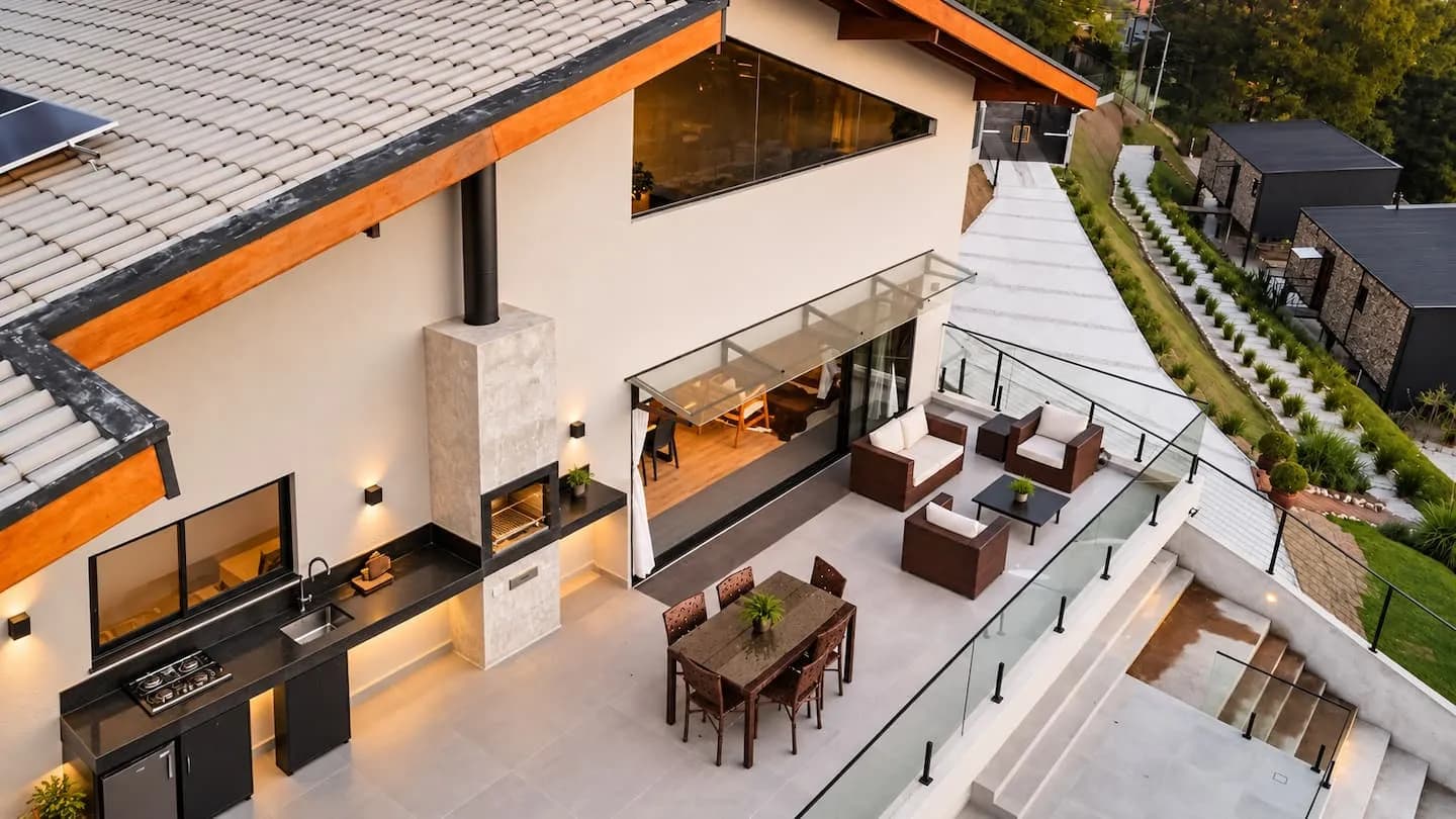 Vista aérea da casa: varanda de vidro, área gourmet com churrasqueira e o terreno em degraus