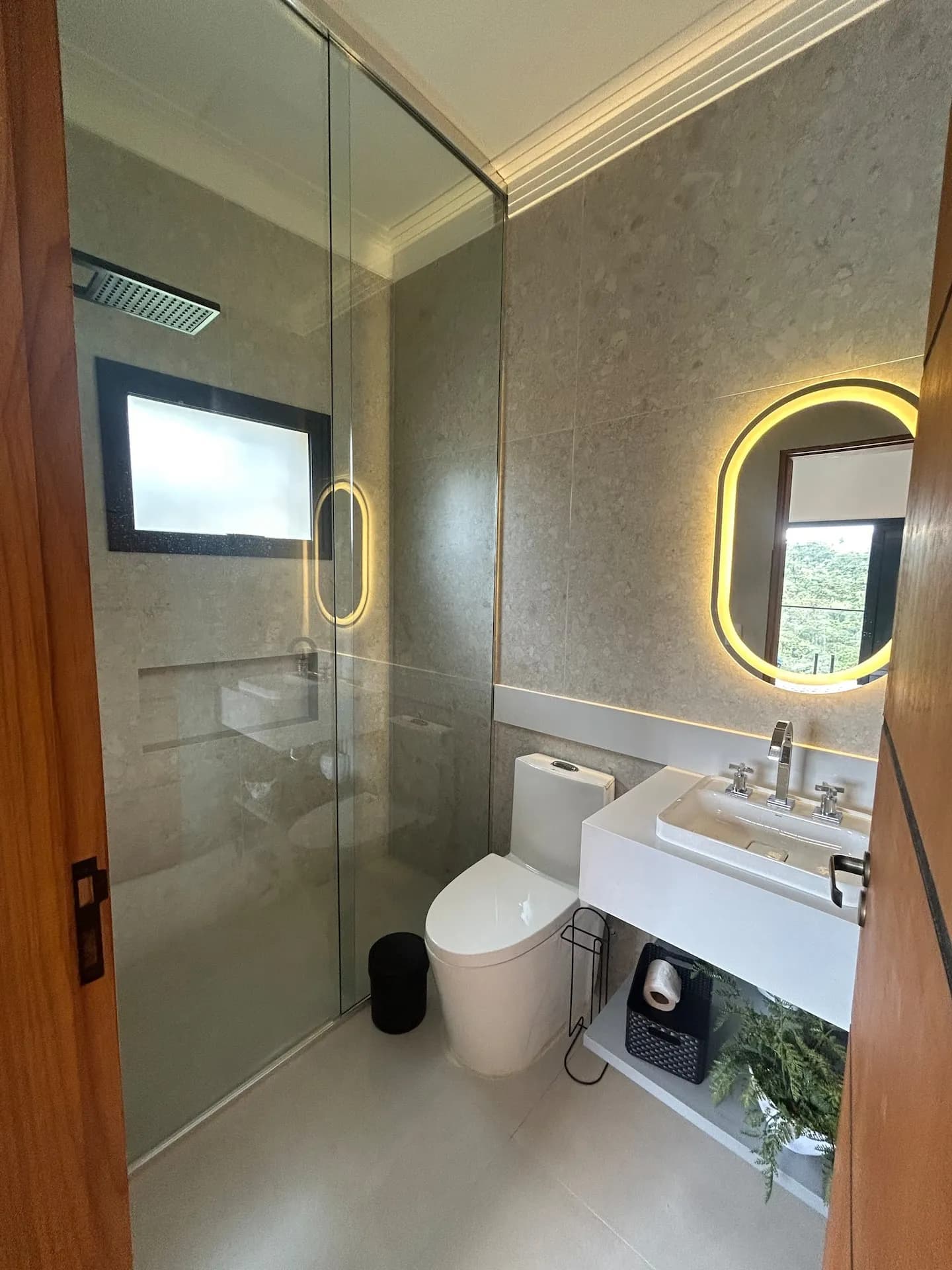 Banheiro de suíte com espelho oval iluminado e box de vidro