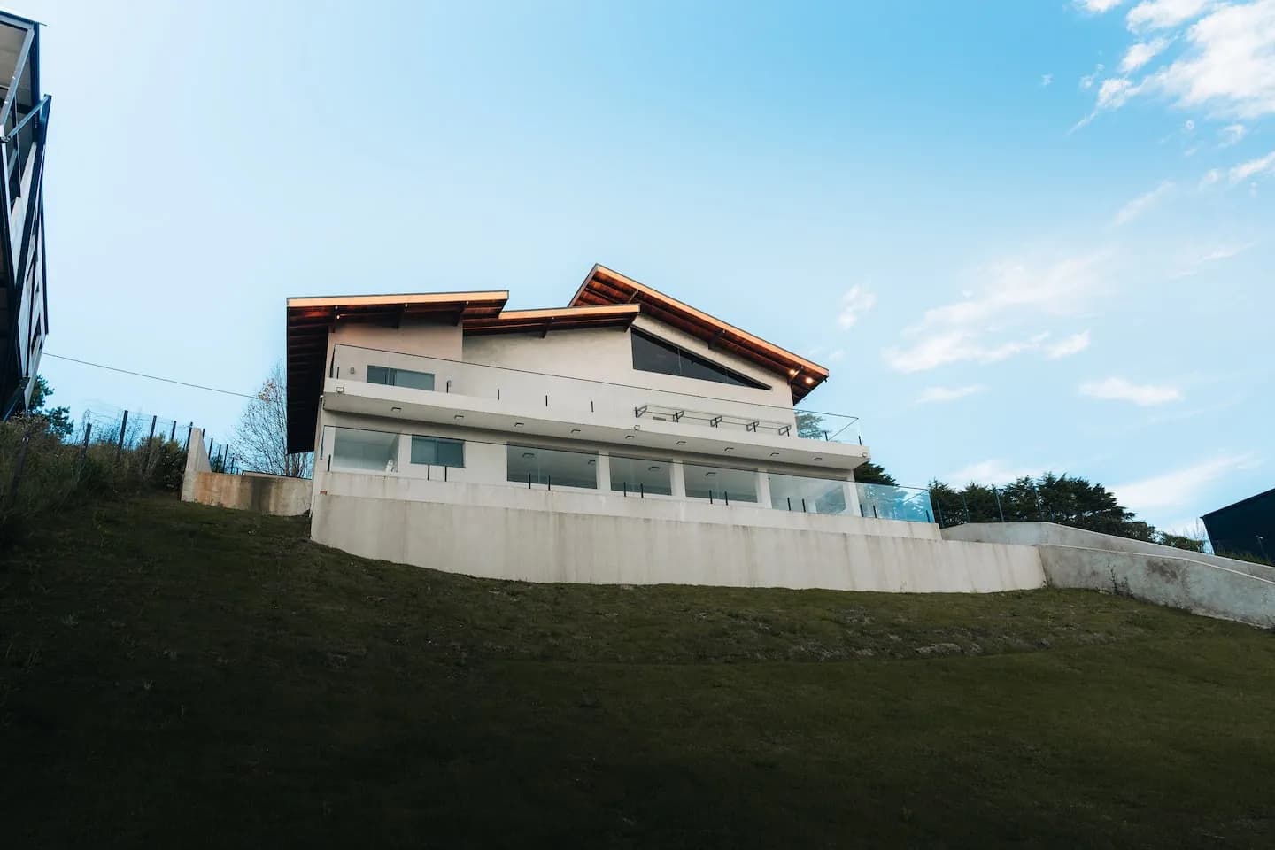 Fachada da casa vista de baixo, com telhado de madeira e vidro sobre o gramado, sob céu azul